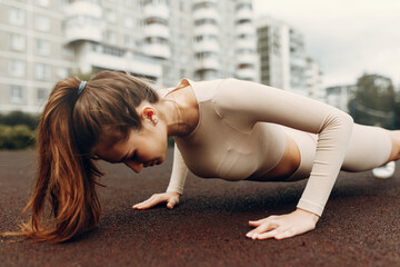 Fototapeta premium A sporty woman trains and exercises at a fitness stadium. Warm-up in the open air, stretching.