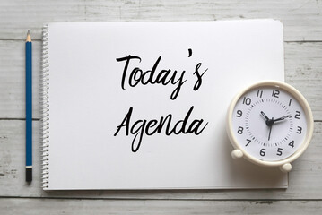 Top view of pencil,clock and notebook written with Today's Agenda on white wooden background.