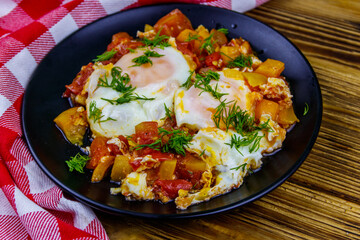 Homemade breakfast shakshuka - fried eggs, onion, bell pepper, tomatoes and dill on rustic wooden table. Jewish cuisine
