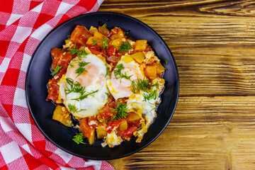 Homemade breakfast shakshuka - fried eggs, onion, bell pepper, tomatoes and dill on rustic wooden table. Jewish cuisine. Top view