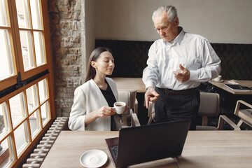 Senior with a young assistant. Businessman working in the cafe. Man in a white shirt. Young woman with her boss.