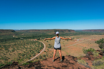 Tourist observing the landscape. Woman wearing shorts, t shirt, trekking boots and a cap. Open arms position. Hiking at Elsey national park, Victoria river, Northern Territory NT, Australia