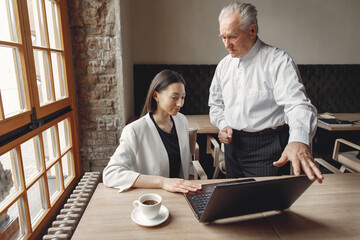 Senior with a young assistant. Businessman working in the cafe. Man in a white shirt. Young woman with her boss.