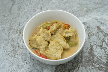 Thai food fish ball in green curry with egg plants and sweet basils in white bowl.
