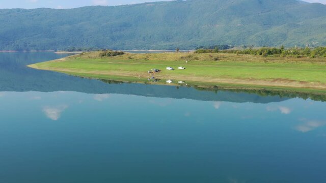 Cars parked on Rama Lake shore in Bosnia and Herzegovina with small campsite, Aerial dolly in shot