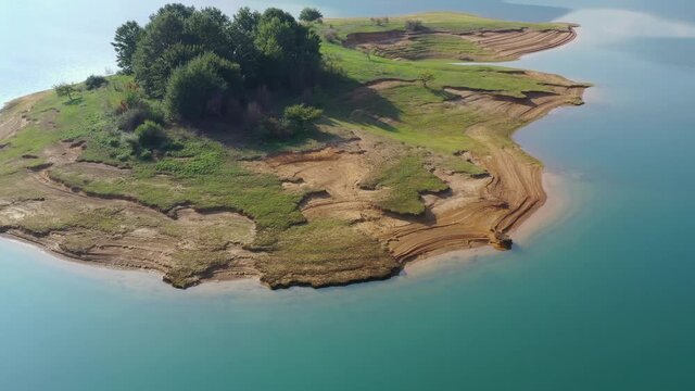 Rama Lake eroded island in Bosnia and Herzegovina with patch of trees, Aerial flyover shot