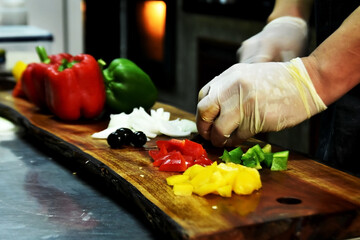The chef cutting fresh red, orange, green and yellow sweet bell paprika on wood cutting board in kitchen room. Raw material for food is important trick and necessary as attract to customer.