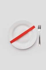 Image of a white empty plate with a red ribbon. A symbol of diet, fasting, or medical fasting. The lack of food.food ban sign