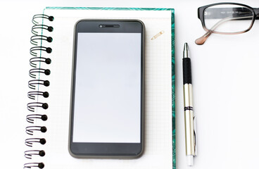 Workspace, on the office desk is a notebook, phone and glasses.