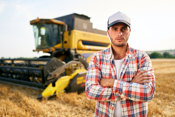 Portrait of proud harvester machine driver with hands crossed on chest. Farmer standing at his...