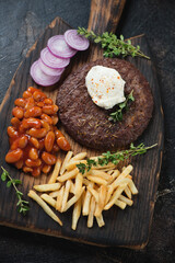 Grilled serbian pljeskavica with kajmak cheese, prebranac, fries and red onion on a rustic wooden serving board, vertical shot