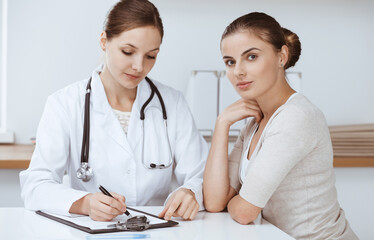 Fototapeta premium Doctor and patient are sitting and discussing health examination results in clinic office. Health care, medicine and good news concepts