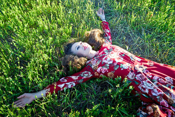 Beautiful woman or girl with magnificent figure laying on the glass in green and yellow field in the setting sun during sunset with warm yellow light. © keleny