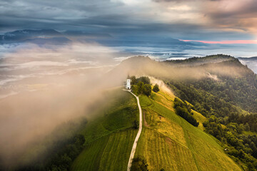 Jamnik, Slovenia - Aerial drone view of a foggy summer sunrise at Jamnik St.Primoz church. The fog...