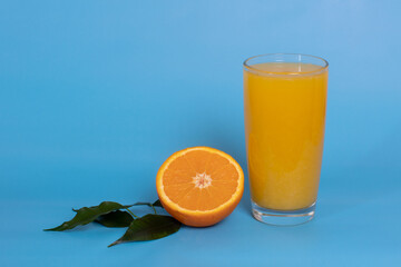 Orange juice in a glass, half an orange with leaves on a blue background. The concept of summer drinks. Copy space