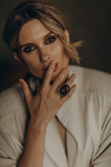 portrait of a stylish blonde woman in elegant totall beige look leather trench coat, ring, and smoky eyes makeup in the studio. Spring - autumn fashion concept. Soft selective focus.