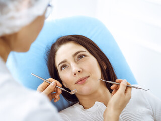 Smiling brunette woman being examined by dentist at dental clinic. Hands of a doctor holding dental instruments near patient's mouth. Healthy teeth and medicine concept