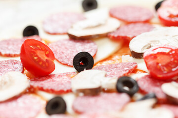 Raw pizza dough with olive over mozzarella, tomato and salami cooking