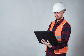 Builder with a laptop. Engineer holds a laptop in his hands. Man in an orange vest and hard hat. Place for an inscription on the wall. Concept - a builder is looking on the Internet. Architect