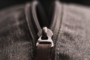 Closeup opened zippers with metal slider body with leather pull tab of gray cloth bag