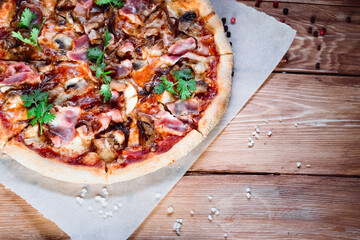 Appetizing pizza on a wooden table surrounded by herbs and spices. The concept of delicious food, restaurants and cafes