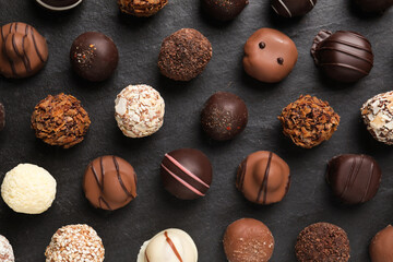 Different delicious chocolate candies on black table, flat lay