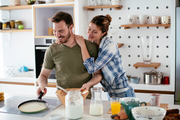 Fototapeta na wymiar Young couple making pancakes together at home. Loving couple having fun while cooking. 