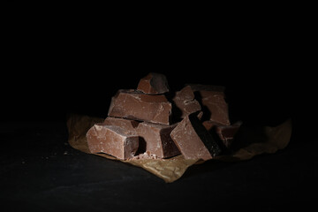 Pieces of tasty milk chocolate on black table, closeup