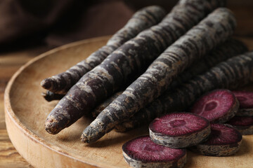 Raw black carrots on wooden plate, closeup