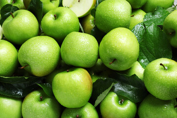 Pile of wet green apples with leaves as background, closeup