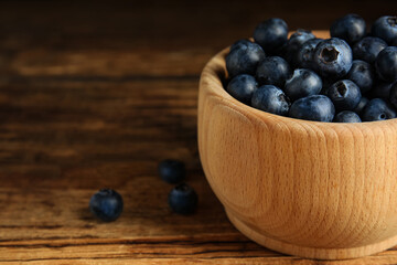 Fresh ripe blueberries in bowl on wooden table, closeup. Space for text