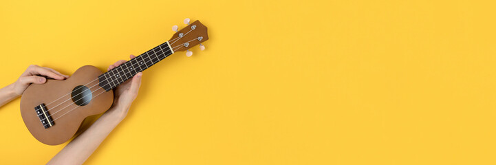 Obraz na płótnie Canvas Female hands hold ukulele on a yellow background. Education the play on hawaiian guitar concept.