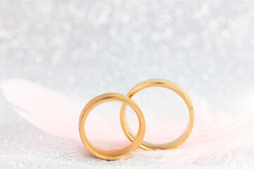 Obraz na płótnie Canvas Golden Wedding Rings and Light Angel Featheron on gentle sparkling background