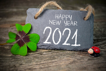 Wooden hang tag and slate with four leaf clover and sparklers with happy new year 2021 on wooden weathered background