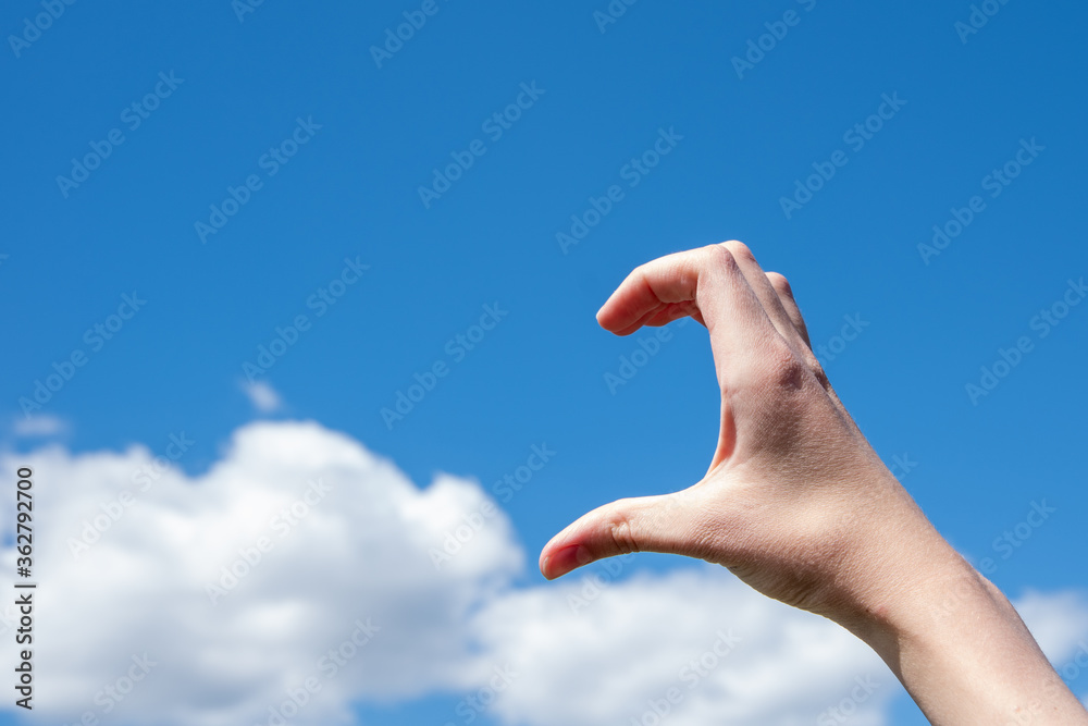 Wall mural Close-up of half heart shaped hand gesture against clouds and blue sky. The concept of loneliness, love. Copy space