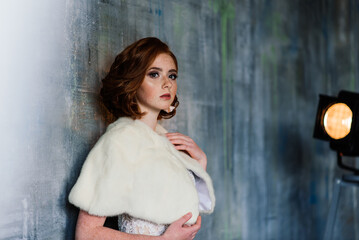 Portrait of red haired girl wearing wedding dress against a white studio background.