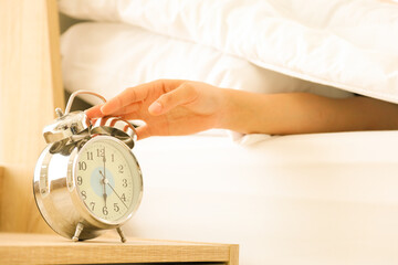 Hand reaching lazily to turn off the alarm clock at 6 am. after wake up in the morning in cozy bed...