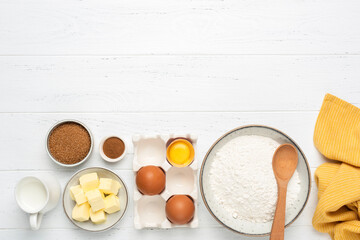Baking ingredients on white wooden table. Ingredients for baking pastry cake or cookies. Bowl of wheat flour, eggs, cubed butter, sugar milk and spices. Top view with copy space for text, design or re - Powered by Adobe