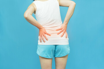 low body of a woman feels back pain wearing  white undershirt standing over isolated blue background with hand on waist because of exercise, painful illness feeling unwell. Ache concept.