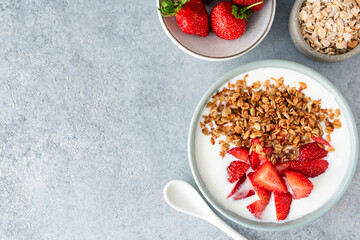 Greek yogurt with granola and strawberries in a bowl on concrete table. Top view, copy space for text or design. Concept of clean eating, dieting