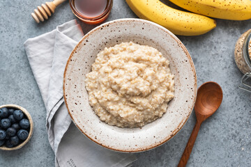 Oatmeal porridge in a bowl served with bananas, blueberries and honey. Top view copy space. Healthy breakfast food, clean eating concept