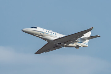 Fototapeta na wymiar White small turbofan-powered business jet airplane flying in the air after takeoff from airport. Fast modern aircraft for air transportation. Aviation technology. Travel and business concept.