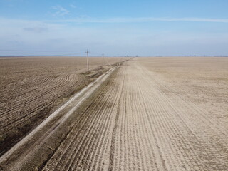 Dirt road between arable fields, aerial view. Landscape. Arable fields in the spring. Power line poles.