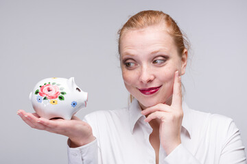 Fototapeta na wymiar young red haired woman looks at her little piggy bank