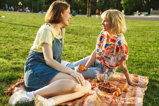 Image of joyful two women laughing and talking while have picnic