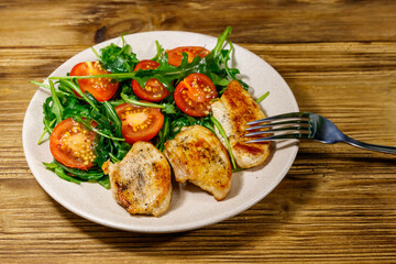 Fried chicken breast with salad of fresh arugula and cherry tomatoes on wooden table