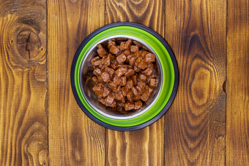 Canned food for cats or dogs in green metal bowl on wooden floor. Top view