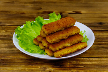 Fried fish fingers on a plate with lettuce on wooden table