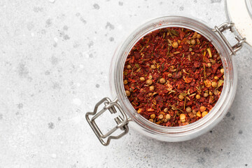 Spice mix: paprika, allspice, coriander, dried tomatoes. A mixture of different spices in a glass jar on the light gray kitchen table. Top view with space for text