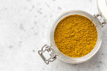 Curry seasoning in a glass jar on the light gray kitchen table. Curry in the jar. Top view with space for text